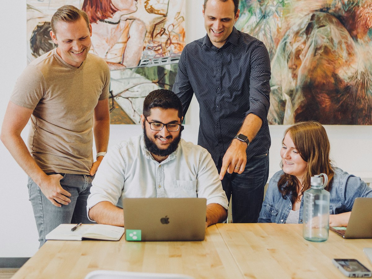 Four colleagues smiling round a laptop
