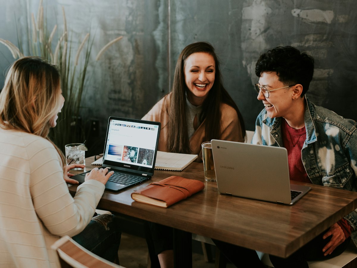 Three people laughing together round a table with laptops
